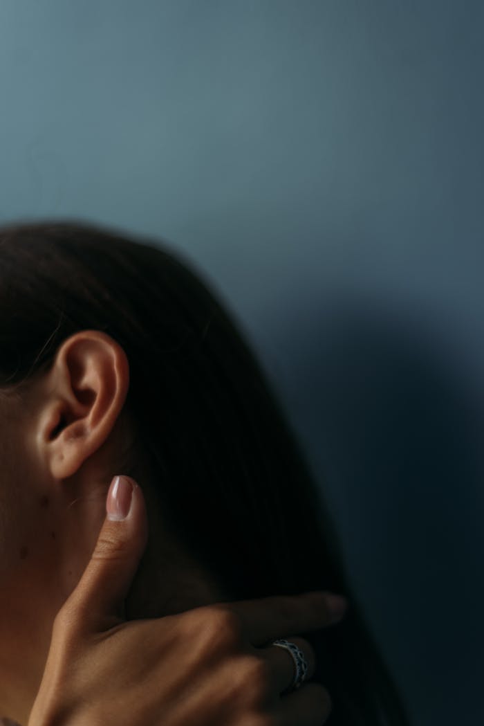 mission-02 Detailed close-up of a womans ear and hand against a moody backdrop, showcasing texture and elegance.