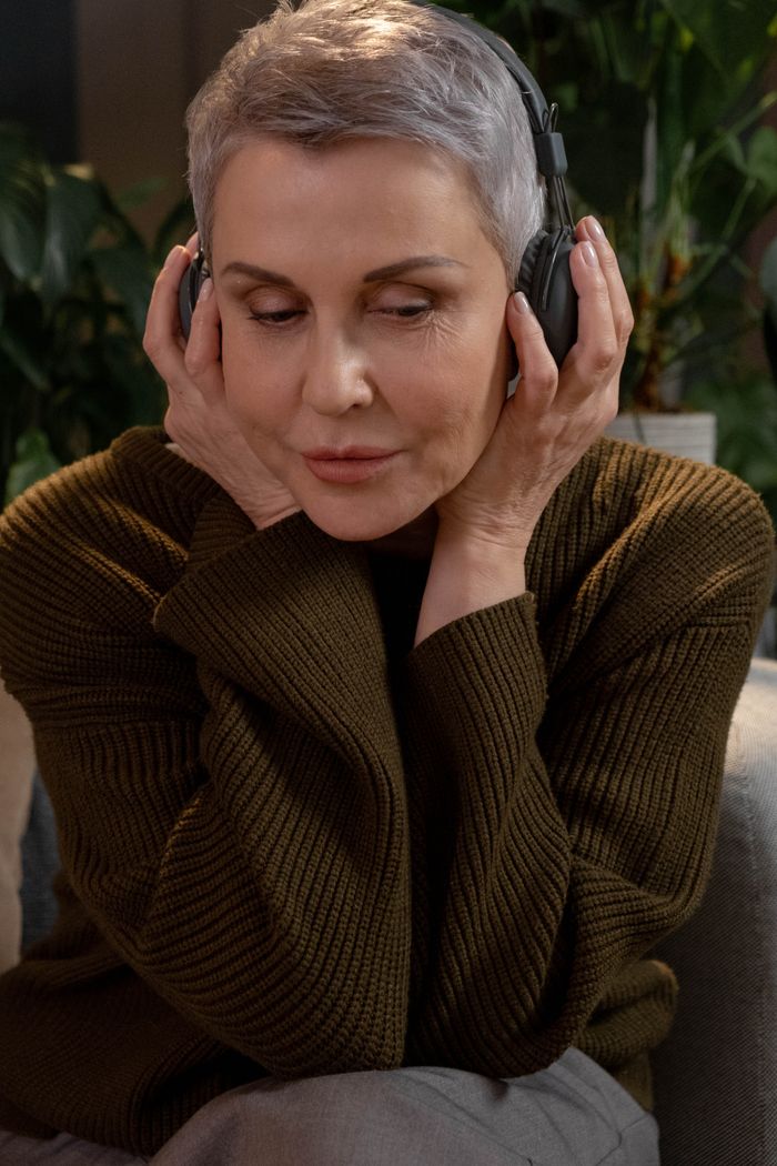 services-01 Mature woman with headphones on a cozy sofa, captivated by music in a peaceful setting.